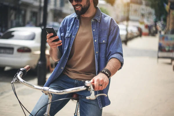 Joven satisfecho sentándose en bicicleta con teléfono — Foto de Stock