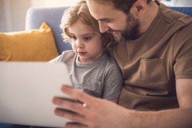 Sırıtan baba ve küçük çocuk laptop bir şey izliyor