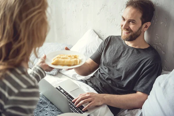 Leende skäggig man blir morgon måltider i sängen — Stockfoto