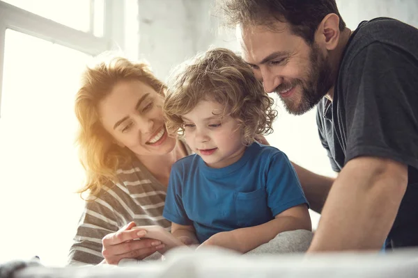 I genitori sorridenti e il bambino stanno guardando lo schermo del telefono — Foto Stock