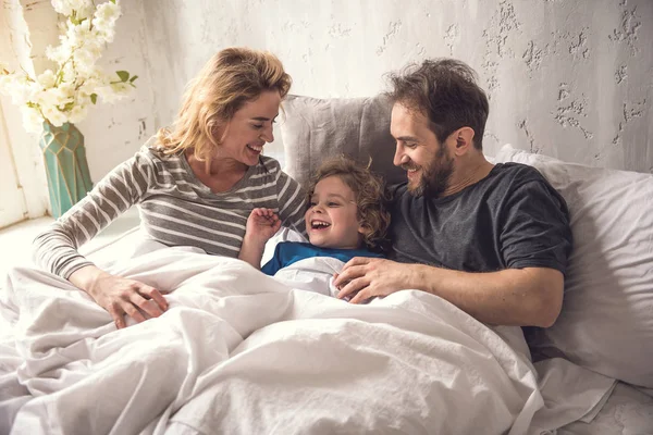 Vrolijke ouders zijn zoon omhelzen tijdens uw verblijf in bed linnen — Stockfoto