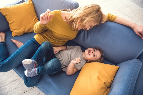 Mamá e hijo se ríen en el sofá en la acogedora sala de estar — Foto de Stock