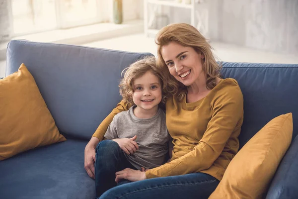 Lycklig mamma kramar grinande liten pojke på soffan — Stockfoto