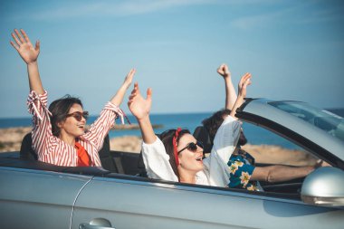 En iyi tatil. Güneş gözlüğü çok memnun genç arkadaşlar yaz yolculuk deniz kıyısı boyunca tadını çıkarıyor. Onlar açık çatı kaldırdı elleriyle arabada oturan ve sevinç ifade. Seyahat kavramı