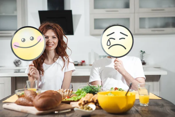 I prefer healthy food. Portrait of joyful young woman is holding happy smile near her face. Man is sitting near her with upset emotion