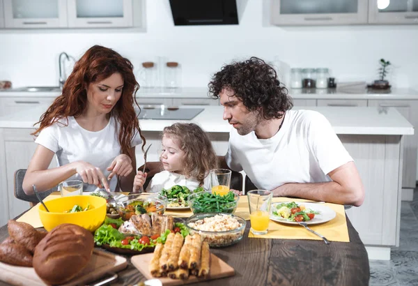 Mom and dad feeding little daughter in kitchen — Stock Photo, Image