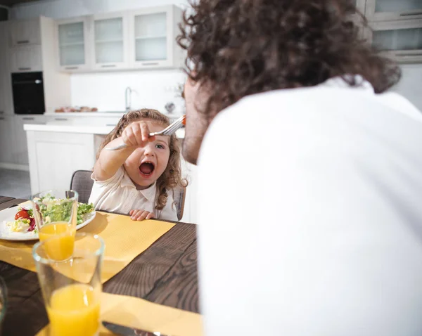 Tată vesel și copil care mănâncă legume în bucătărie — Fotografie, imagine de stoc