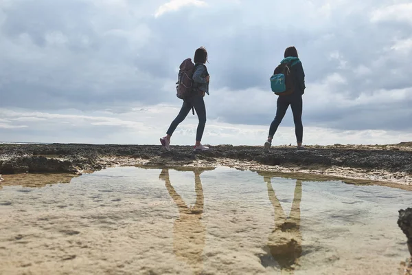 Vrouwelijke toeristen wandelen aan de kust met rugzakken — Stockfoto