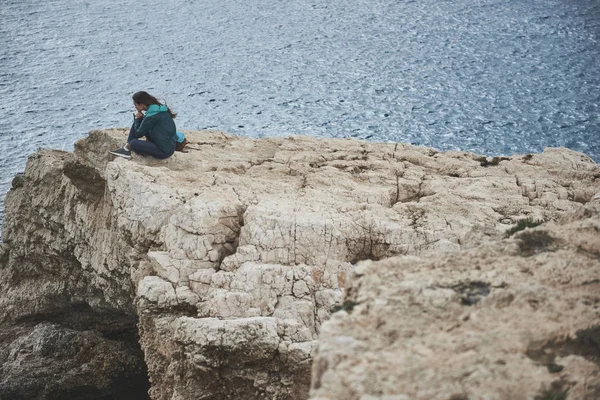 Vrolijk meisje zittend op een klif in de buurt van het water — Stockfoto