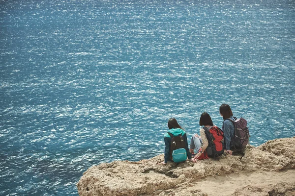 Drie meisjes ontspannen op klif in de buurt van het water rustig — Stockfoto