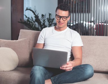 Oturma odasında dizüstü bilgisayarda yazarak memnun erkek serbest meslek 