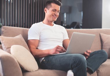 Oturma odasında modern bilgisayar kullanan rahat adam 