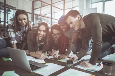 Eğlenceli birlikte. Mutlu genç olumlu erkek ve kadınların modern ofis yerde yatan ve dizüstü bilgisayarda çalışıyor. Yaratıcı sürece dahil sırasında aygıt ekranında arıyorlar