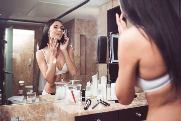 Tevreden vrouw praten over telefoon door looking glass in badkamer — Stockfoto