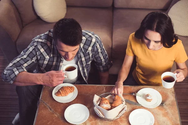Розслаблений молодий чоловік і жінка їдять тістечко з гарячим напоєм — стокове фото