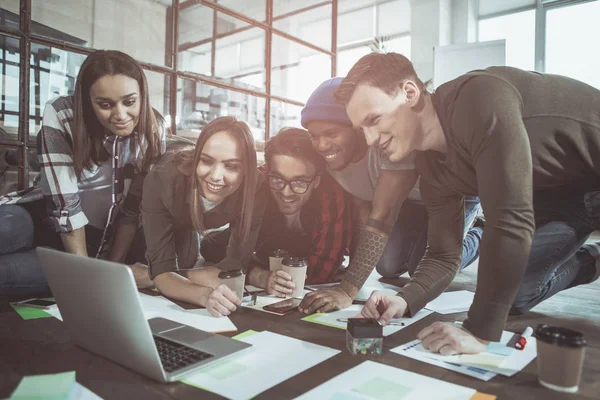Eğlenceli birlikte. Mutlu genç olumlu erkek ve kadınların modern ofis yerde yatan ve dizüstü bilgisayarda çalışıyor. Yaratıcı sürece dahil sırasında aygıt ekranında arıyorlar