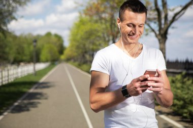 Neşeli adam akıllı telefon ve kulaklık doğada kullanıyor