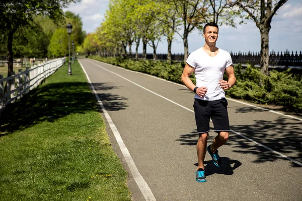 El hombre sonriente está trotando a lo largo de un camino soleado en un ambiente verde — Foto de Stock