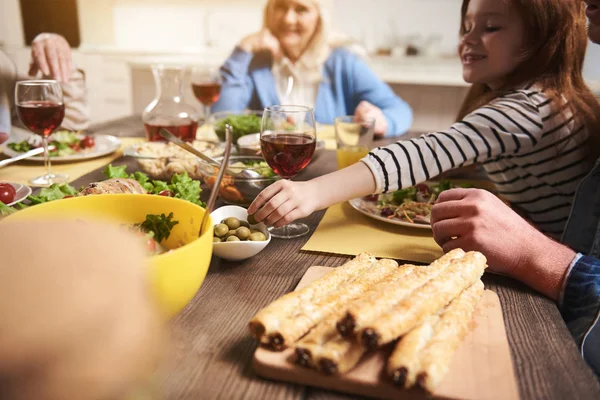 Small delighted girl eating at table with family — Stock Photo, Image