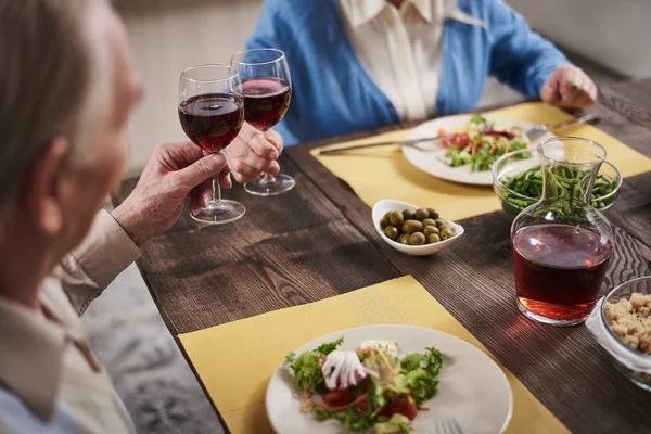 Älteres Ehepaar klirrt mit Gläsern am Tisch — Stockfoto