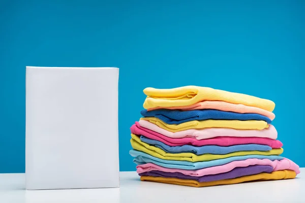 Laundry detergent and clean clothes lying on table — Stock Photo, Image