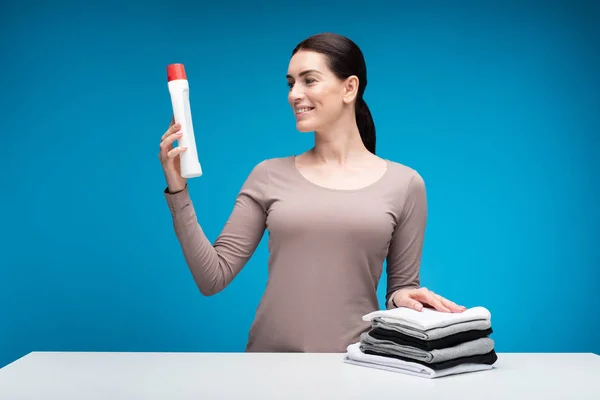 Mulher feliz segurando detergente à mesa — Fotografia de Stock