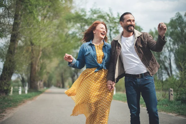 Joyful mature loving couple walking along park alley — Stock Photo, Image