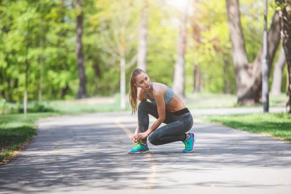 Deportiva mujer está atando zapatos en la carretera —  Fotos de Stock