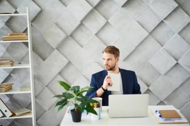 Ciddi ve düşünceli erkek tablet ellerde ile masada oturuyor. Çalışmalarına yansıtan ise yana doğru bakıyor. Saksı, defter ve laptop üstünde okul sırası yalan vardır