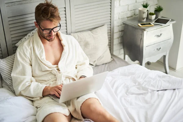 Joven concentrado trabajando en la cama — Foto de Stock