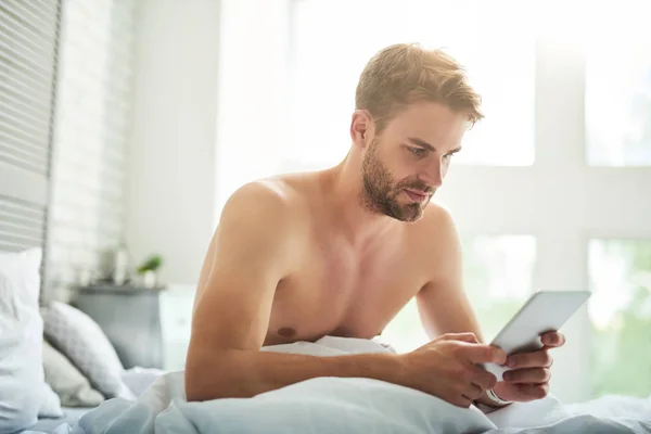 Hombre guapo serio navegando red en la cama — Foto de Stock