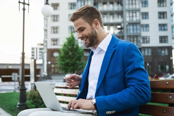 Vrolijke zakenman genieten van online winkelen met laptop in park — Stockfoto