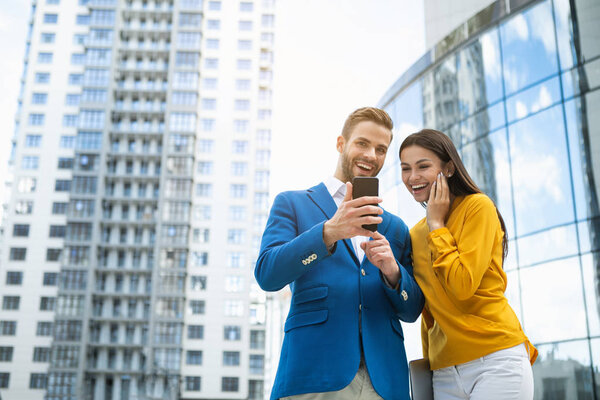 Joyful businessman showing gadget to woman on street 