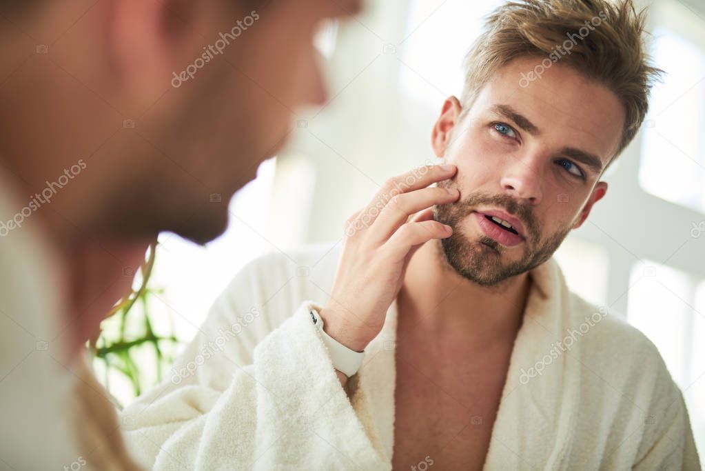 Waist up portrait of male reflection. He is standing and checking on beard going to shave after sleep