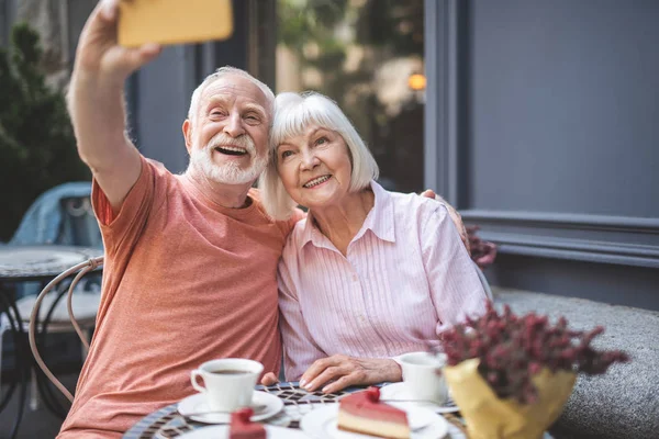 Счастливая пожилая пара делает селфи в кафе — стоковое фото