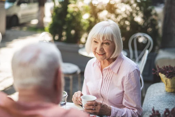 Delighted senior woman talking to man at table