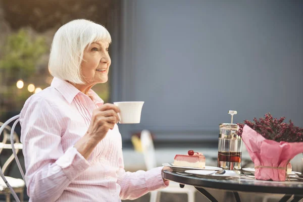 Cheerful senior lady drinking hot drink outdoors — Stock Photo, Image