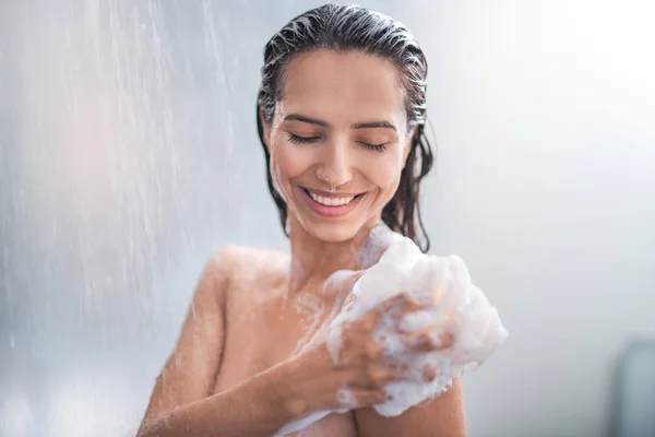 Smiling female rubbing body with foam — Stock Photo, Image