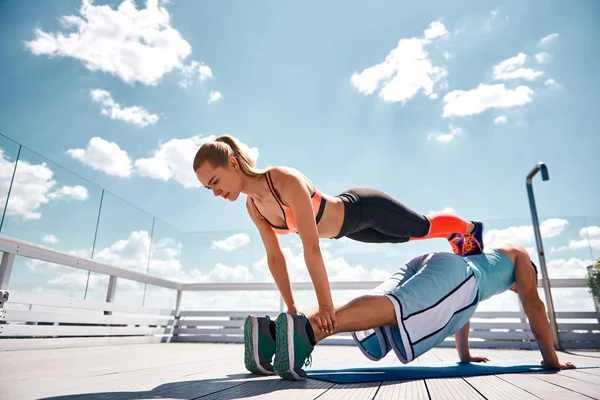 Mujer delgada está haciendo fitness con novio asistencia al aire libre — Foto de Stock