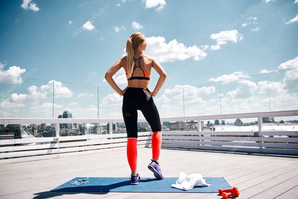 Slim lady is enjoying cityscape during workout on roof