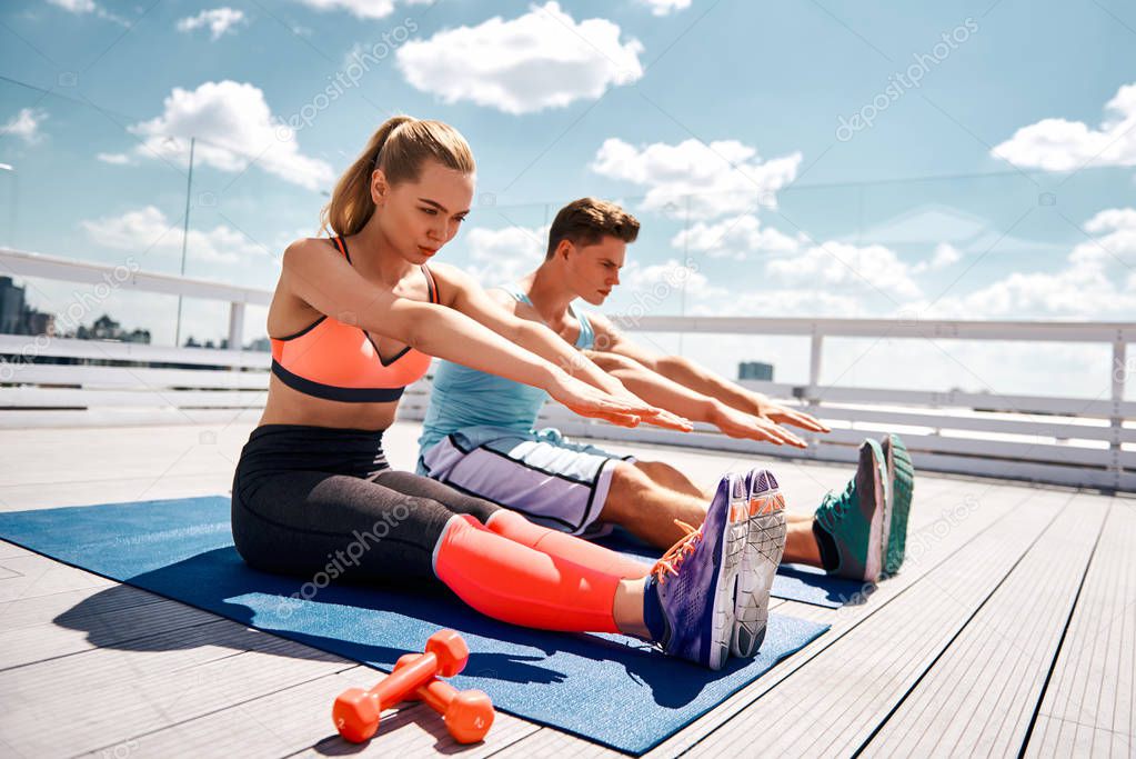 Sporty couple is concentrated on flexibility workout outdoors