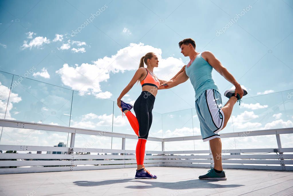 Man and woman are supporting each other while exercising outdoors