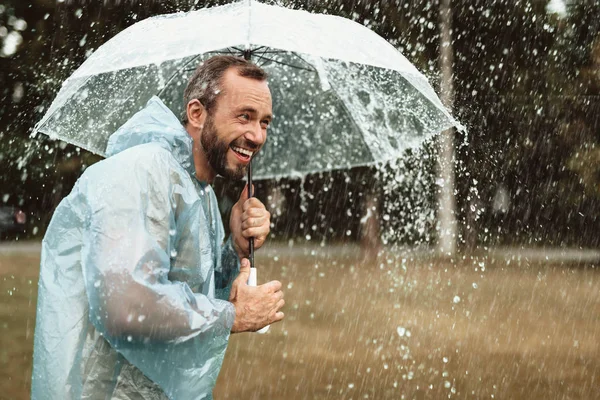 Веселый парень прячется под зонтиком снаружи — стоковое фото