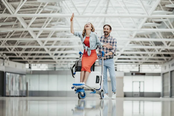 Homme satisfait portant dame sur chariot à bagages — Photo
