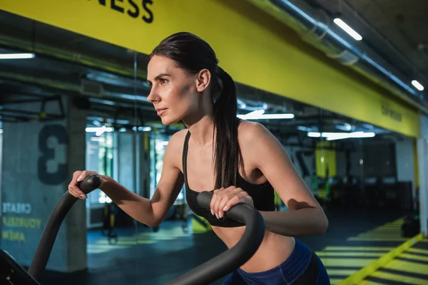 Mujer concentrada está haciendo ejercicio con simulador en el gimnasio —  Fotos de Stock