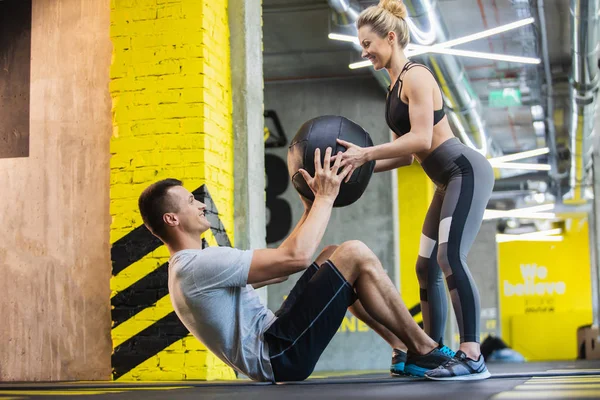 Fröhliche Frau trainiert wohlgeformten Kerl im Fitnessstudio — Stockfoto