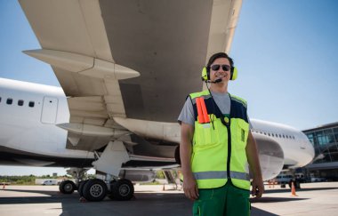 Cheerful airport worker posing near passenger plane clipart
