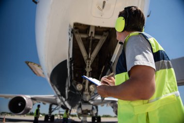Airport worker looking at aircraft while holding pen and checklist clipart