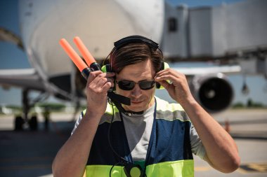 Aviation marshaller touching sunglasses while holding signal wands clipart