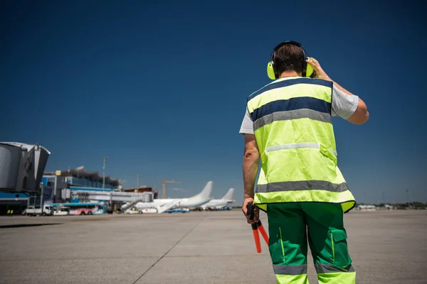 Flygplats arbetaren röra hörlurar och tittar på airdrome — Stockfoto